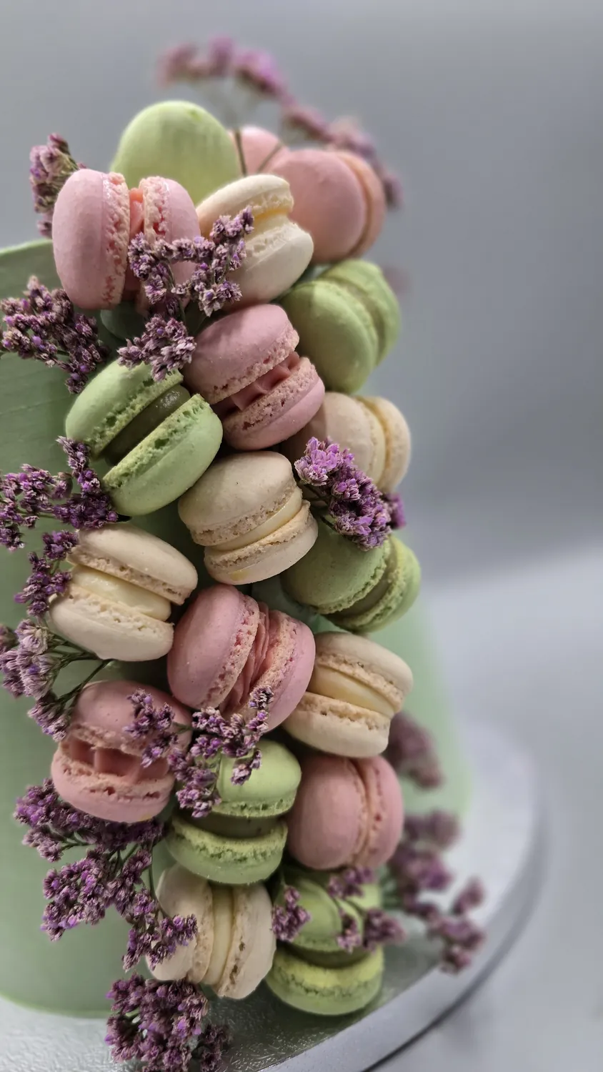 Hohe Torte, üppig verziert mit bunten Pastell-Macarons und lila Blüten