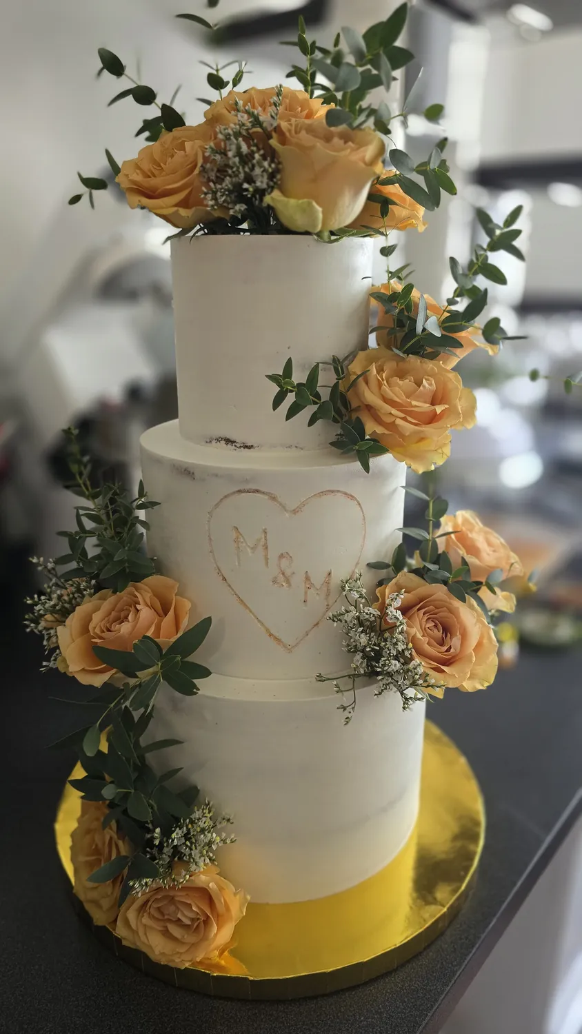 Dreistöckige Hochzeitstorte dekoriert mit orangefarbenen Rosen und goldenen Initialen